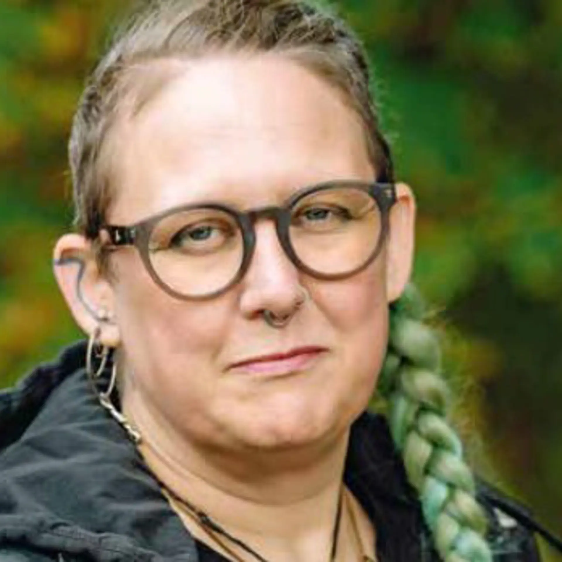 Kvinna med lång fläta över axeln, glasögon och mörk jacka ser in i kameran. 