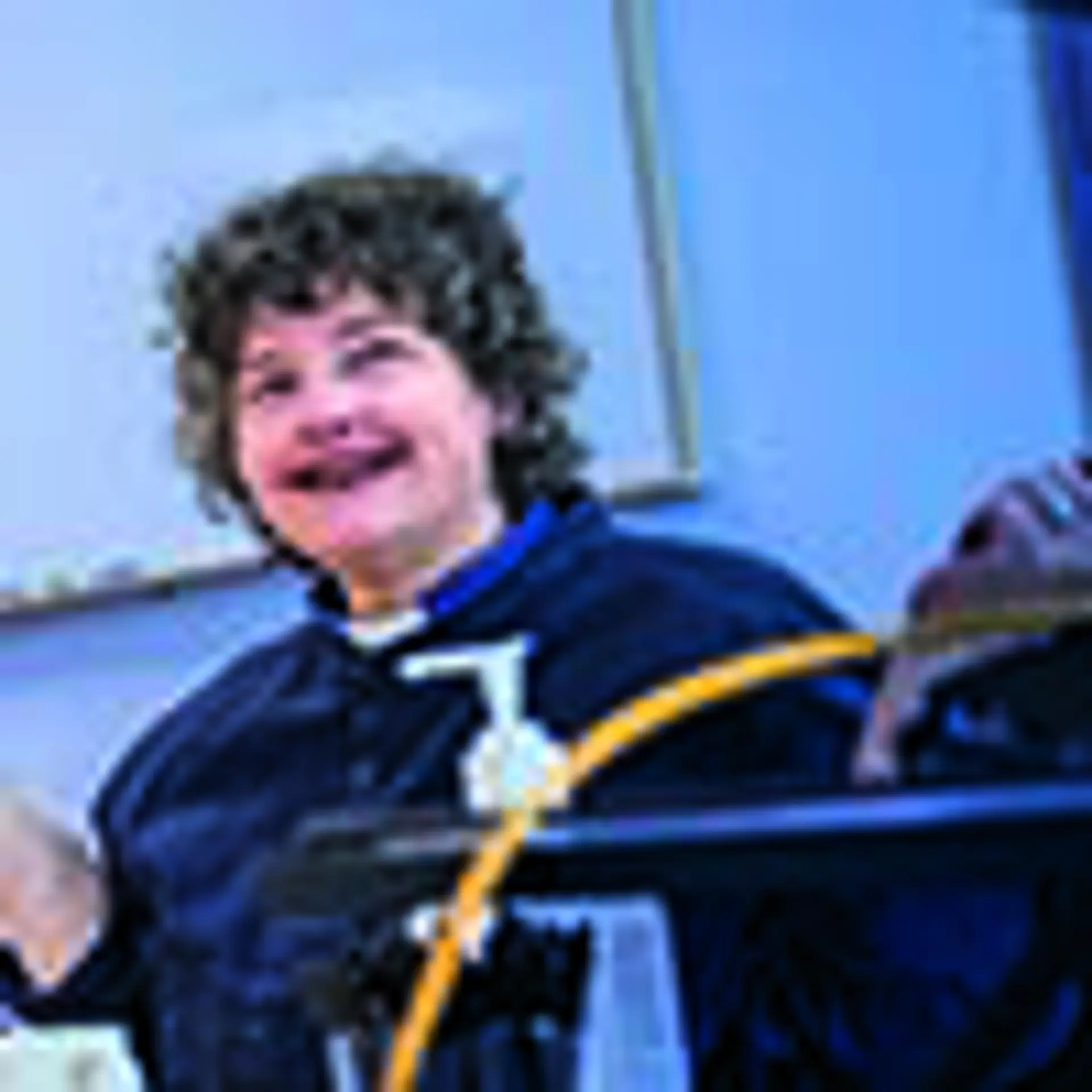 Kvinna med lockigt hår och prästskjorta ler