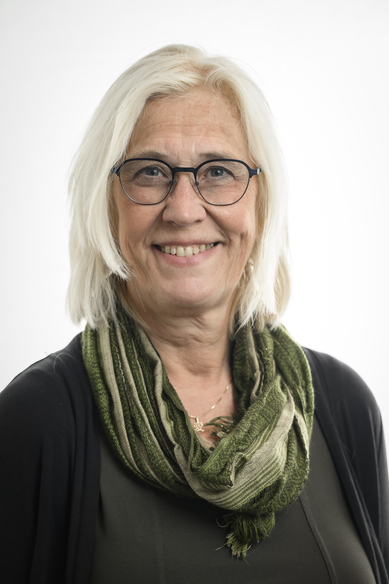 Kvinna med ljust hår och mörka kläder samt glasögon tittar in i kameran och ler. 