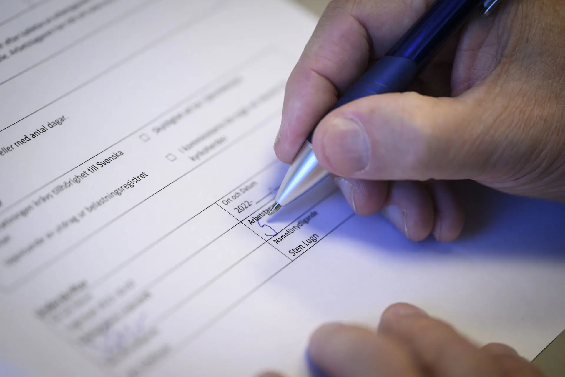 Person håller i en bläckpenna med höger hand och skriver under ett anställningsavtal