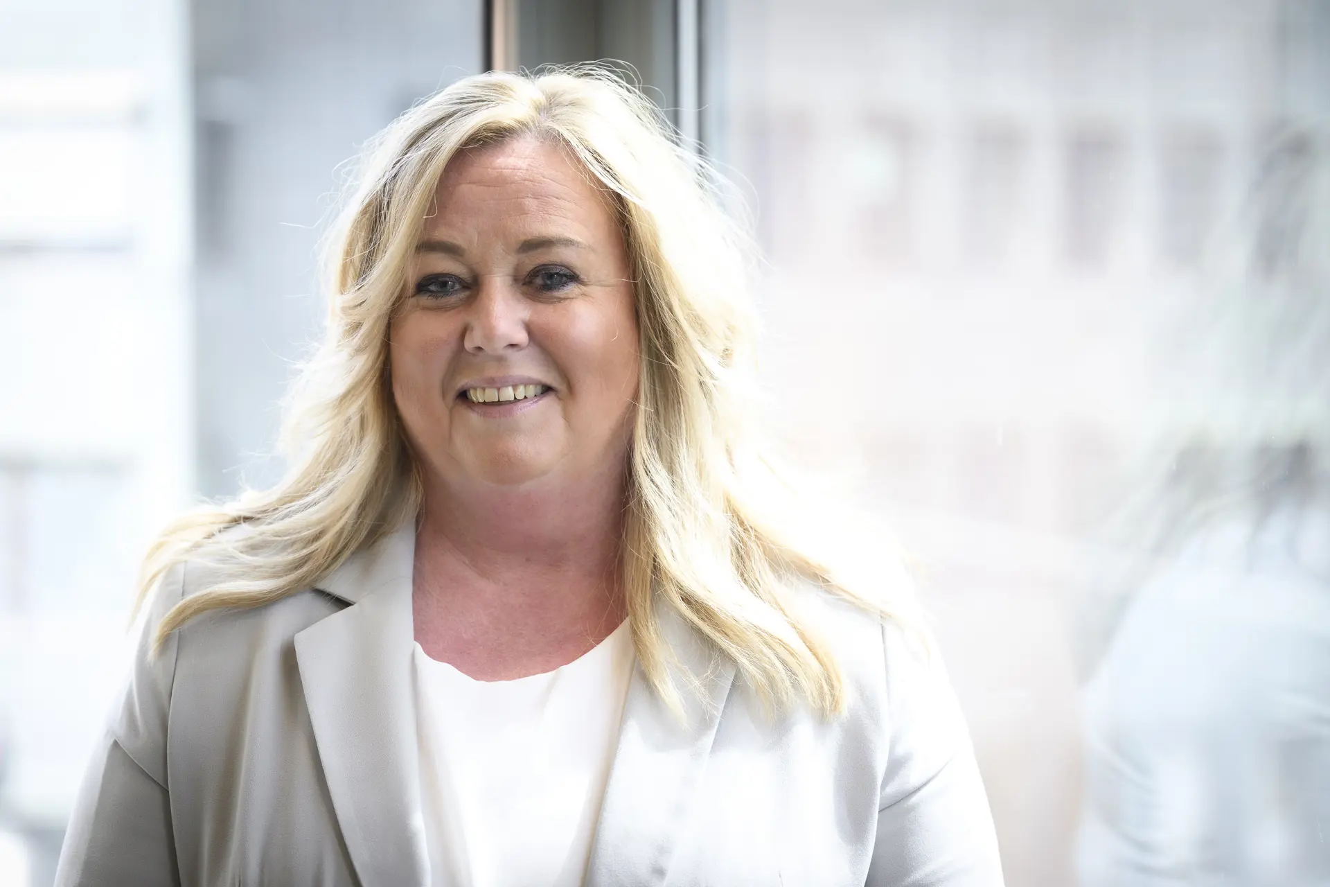 Kvinna i ljusa kläder och axellångt ljust hår tittar in i kameran och ler.