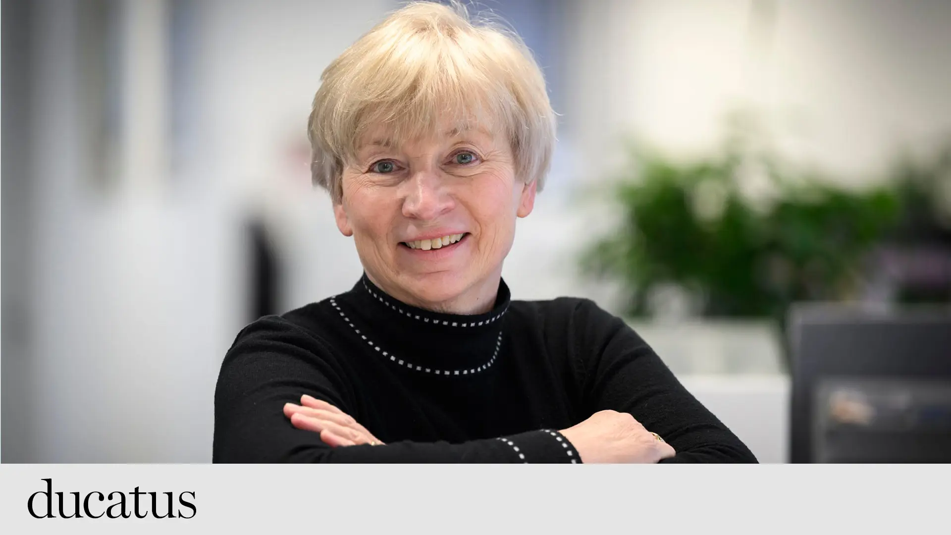 Kvinna med kort ljust hår och armarna i kors tittar in i kameran och ler. 