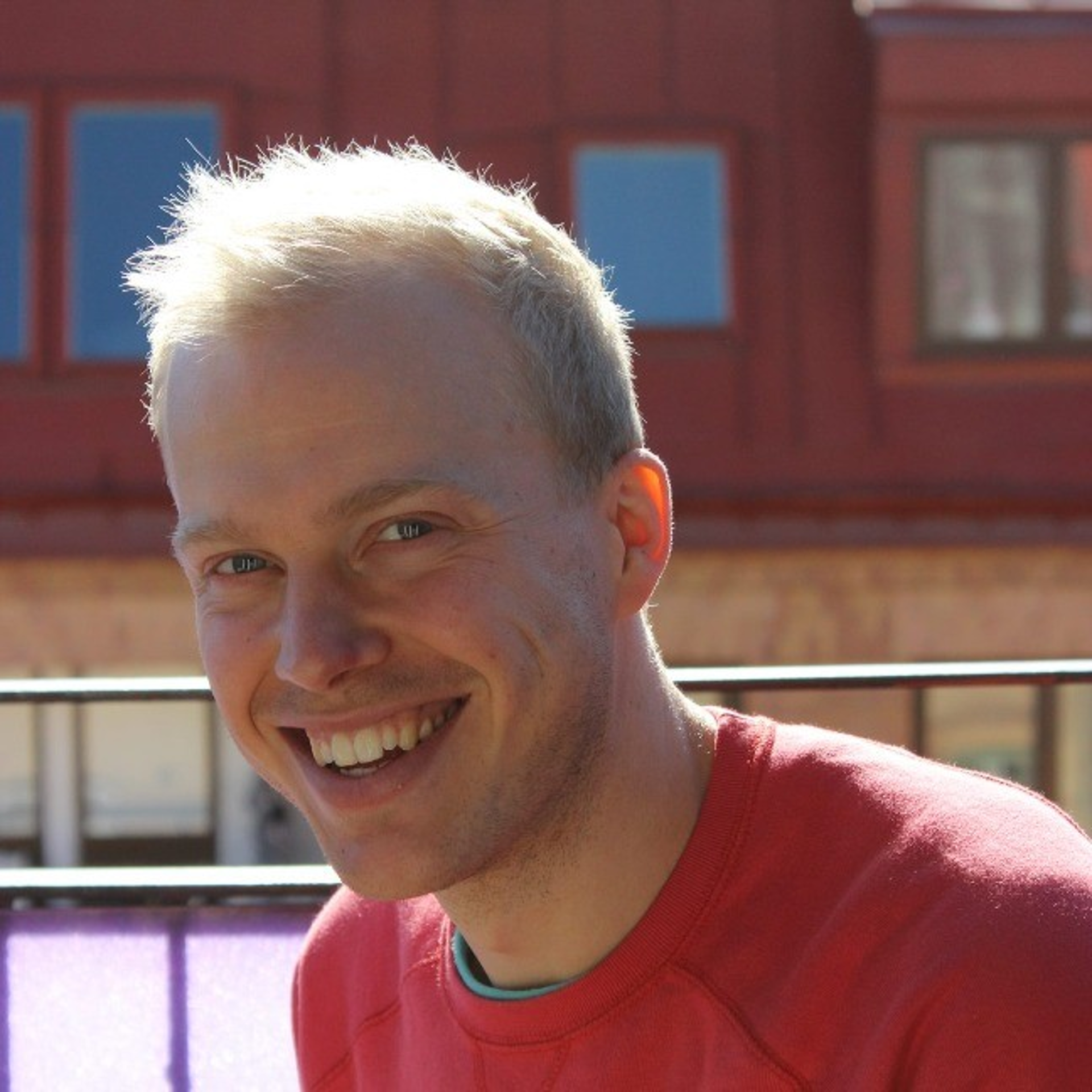 Man med ljust kort hår och orange tröja tittar in i kameran och ler. 